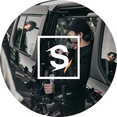 Michi (Michael Schanz), one of your two hosts, with a camera rig at a car door – round portrait with the white Spreadfilms S signet