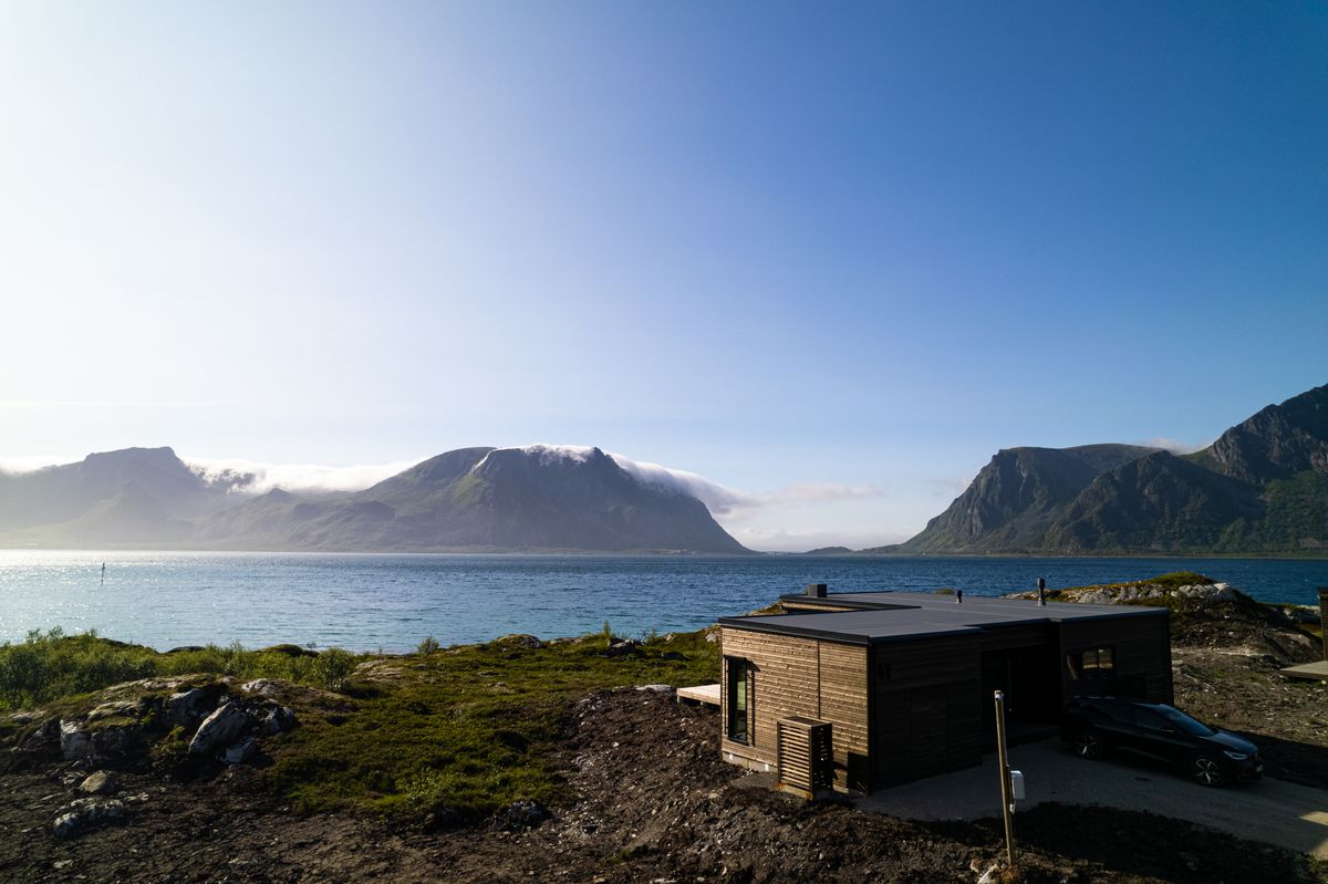 The Lyngvær house above the fjord on a sunny day, mountains across the water