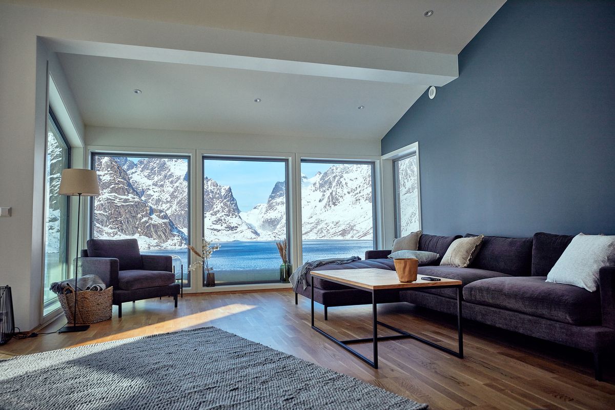 Lounge in Reine with a large sofa and a rug, snowy mountains through three windows
